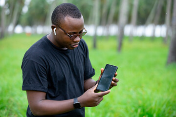 Young African Agricultural Engineer using a blank screen smartphone in an agricultural field. for monitoring plant growth.