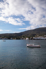 Barco blanco en medio del mar del pueblo de Cadaqués con el pueblo y la verde montaña de fondo...