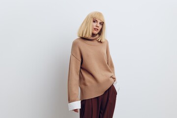 Horizontal photo, a woman on a white background in a beige sweater and brown trousers with beautiful blond hair is standing