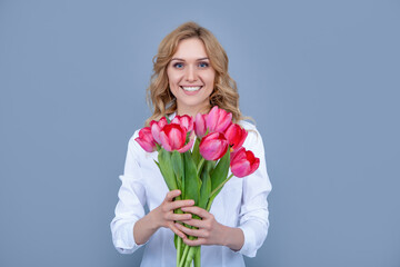 glad blond woman with spring tulip flowers on grey background