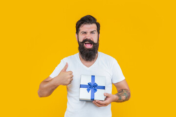 winking man with present isolated on yellow background. present box for man in shirt. birthday man