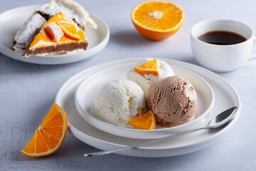 Vanilla and chocolate ice cream, cake and orange slices on a light wooden table