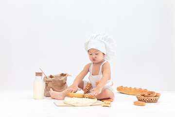 A cute Asian child in an apron and a chef's hat is preparing pastries from dough. Place for text.