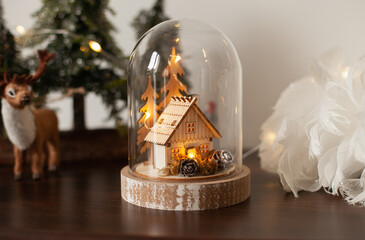 Glass cloche with a wooden house inside and golden lights. Christmas decoration at home. Festive...