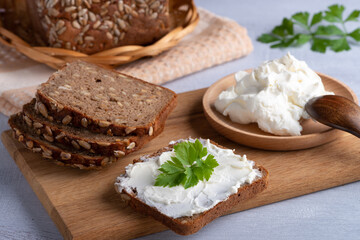 Home made rye bread on a wooden cutting board with curd cheese, ricotta and herbs.