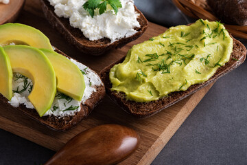 Sandwiches with a minced curd, avocado and herbs on the natural wooden cutting board. Healthy food concept
