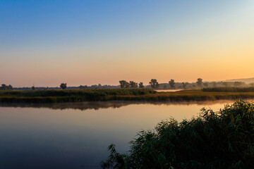 Naklejka premium View of river in the mist at sunrise. Fog over river at morning