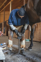 Busy European blacksmith in work clothes shoves back hoof of brown horse