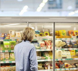 Man choosing frozen food from a supermarket freezer., reading product information