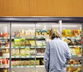  Man choosing frozen food from a supermarket freezer., reading product information