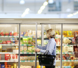 Man choosing frozen food from a supermarket freezer., reading product information