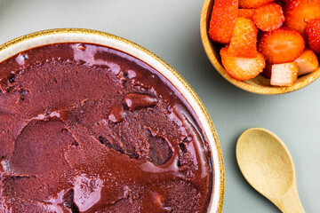 Brazilian açai in a white bowl, additional strawberry, granola and nuts in small bamboo bowls. Cashew nuts and Pará. Top view. Grey background. Selective focus