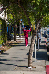 an African American woman with long hair wearing a red sweat suit walking along a sidewalk lined...