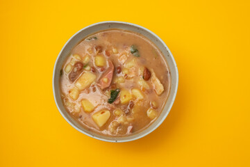 Sopa de pedra Portuguese Stone Soup with beans and sausages in the plate on yellow.