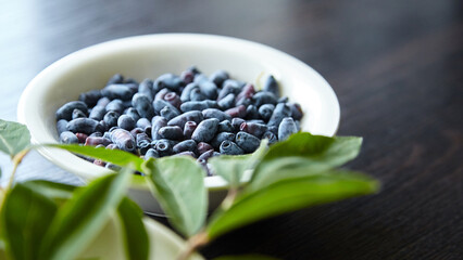 Fresh honeyberry (Lonicera caerulea) in white bowl on wooden table. Blue haskap berry with green...