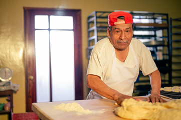 Retrato de un hombre adulto feliz trabajando en una panaderia. Hombre Latino haciendo Shecas, pan, pasteles, galletas, pizza artesanales.  - obrazy, fototapety, plakaty