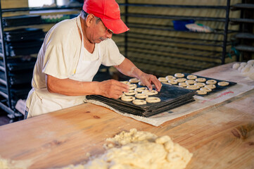 Hombre trabajando con masa y harina de trigo en una panaderia artesanal. Hombre Latino en una panaderia. - obrazy, fototapety, plakaty
