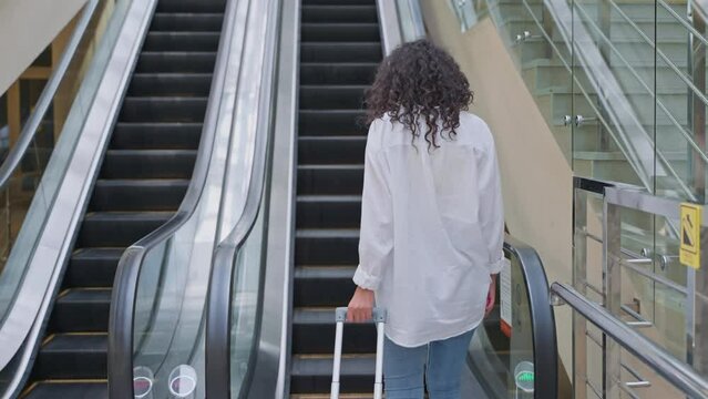 Woman traveler with luggage on escalator going up