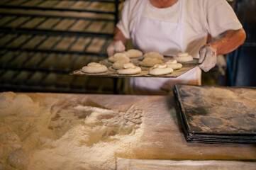Retrato de un hombre adulto trabajando en una panaderia. Hombre haciendo Shecas, pan, pasteles, galletas, pizza artesanales.  - obrazy, fototapety, plakaty