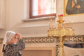 a little Christian girl in an Orthodox church puts a candle, prays in front of the icon. High quality photo