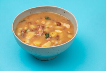 Sopa de pedra Portuguese Stone Soup with beans and sausages in the plate on blue.