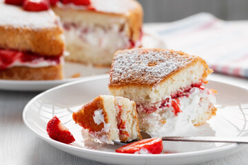 Eating a piece of Victoria biscuit cake with whipped cream, jam and fresh strawberries