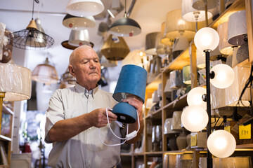Elderly man looking for new table lamp at store of household goods