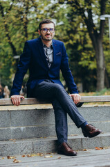 A man in a suit is sitting on a bench in the park