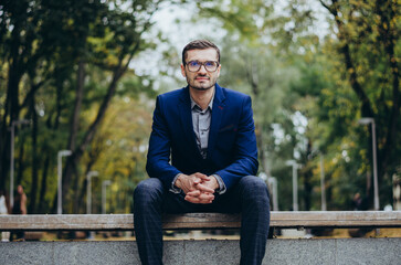 Obraz premium A man in a suit is sitting on a bench in the park