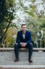 A man in a suit is sitting on a bench in the park