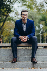 Obraz premium A man in a suit is sitting on a bench in the park