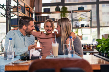 lovely cuddling moment between mom, dad and their little daughter, while they waiting for their lunch in the restaurant. Family time concept.