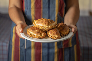 Woman in apron holding a tray with Argentine empanadas.