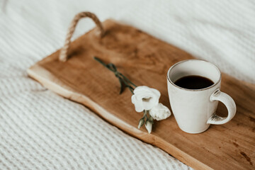 Cup of black coffee on wooden tray in bed with white flower - perfect birthday surprise