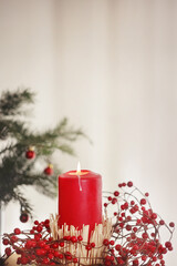 Lit red candle in Christmas wreath white background copy space