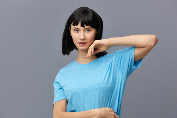 Obraz premium a peaceful woman stands on a dark background in a blue T-shirt, raised her elbow up, leaning her fingers against her face, putting the second fart on her stomach