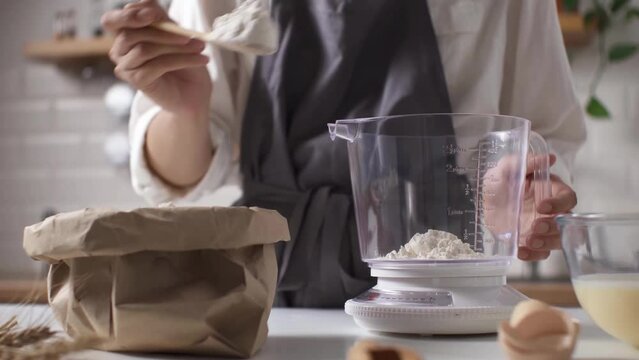 Baking home baker in special clothes in an apron weighs flour with kitchen mechanical scale, giving the correct proportion according to the recipe Process of preparing dough for baking a flour product