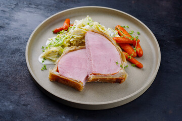 Gebackenes Kasseler Schweinesteak im Teigmantel mit Wirsing Kohl und Baby Karotten serviert als close-up auf einem Design Teller mit Textfreiraum