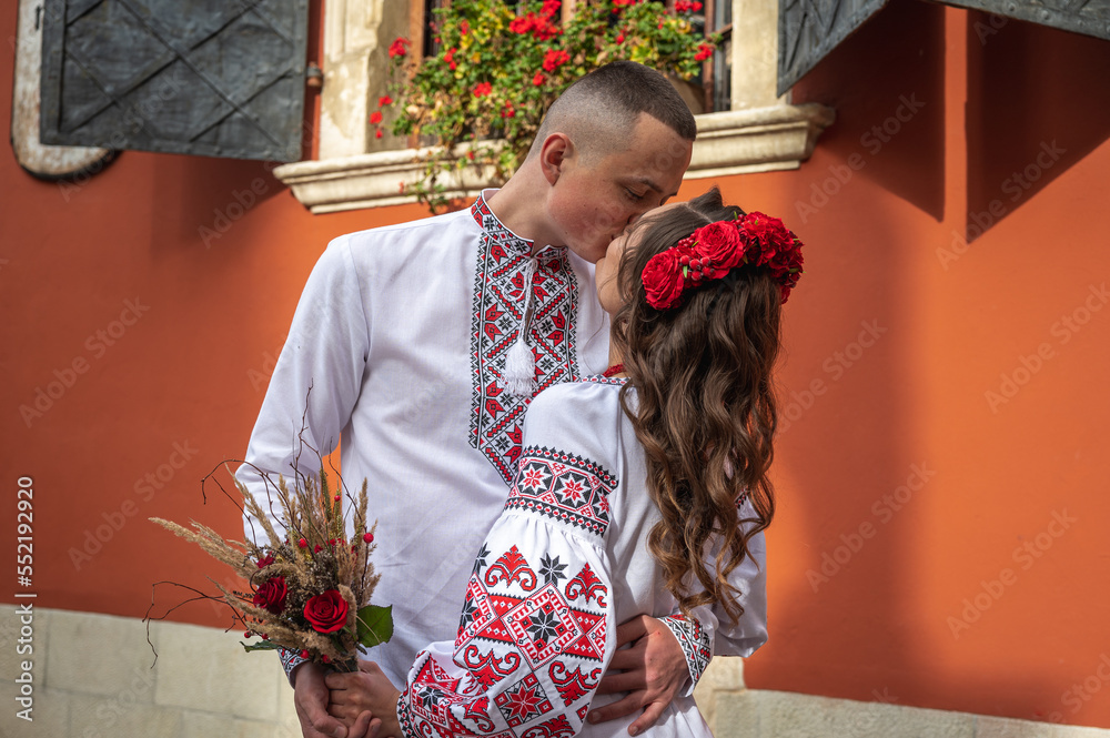 Wall mural A happy young couple in love, a family walking through the old city of Lviv in Ukrainian embroidered dresses, holding hands. Young people hug in the old town of Lviv
