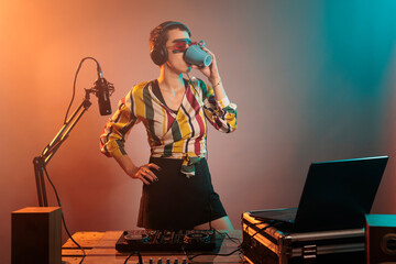 Cool DJ artist drinking coffee from mug before mixing techno music, preparing to do performance on...