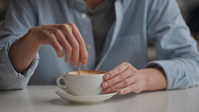 Close-up of a cup of cappuccino with foam, a girl sits in a restaurant, slowly drinks coffee, stirs with a metal spoon a thick foam of whipped milk for coffee, a white cup for a hot drink
