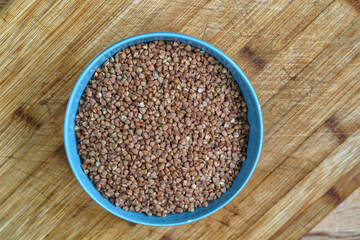 Buckwheat in a bowl on wooden background, top view.