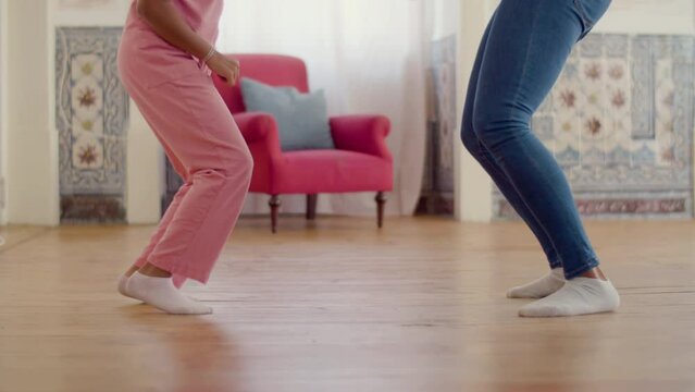 Legs closeup of mum and daughter dancing at home in white socks. Happy African American woman and her child having fun together, jumping and moving to music. Slow motion. Leisure, parenthood concept.
