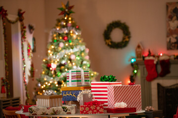 Christmas gifts piled up on a table in front of a Christmas Tree in a family room.