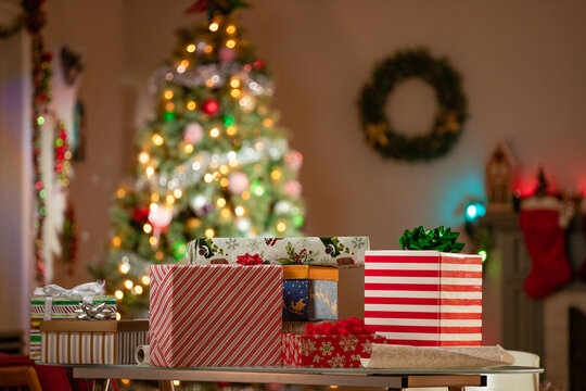 Christmas gifts and loose wrapping paper on a table in front of a Christmas Tree in a family room.