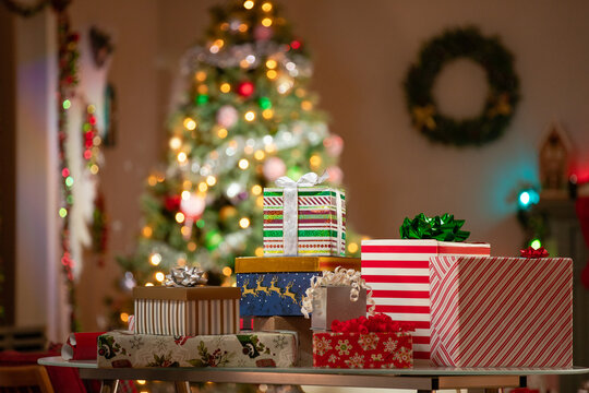 Christmas gifts arranged on a table in front of a Christmas Tree in a family room.