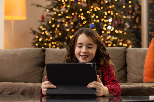 Smiling ten year old girl FaceTiming on an iPad in a living room in front of a Christmas Tree