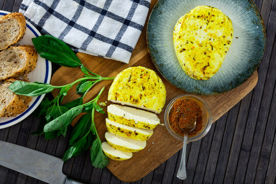 Slices of spicy roasted cottage cheese seasoned with turmeric and cumin seeds on wooden cutting board served with whole-grain baguette and greens. Healthy breakfast concept
