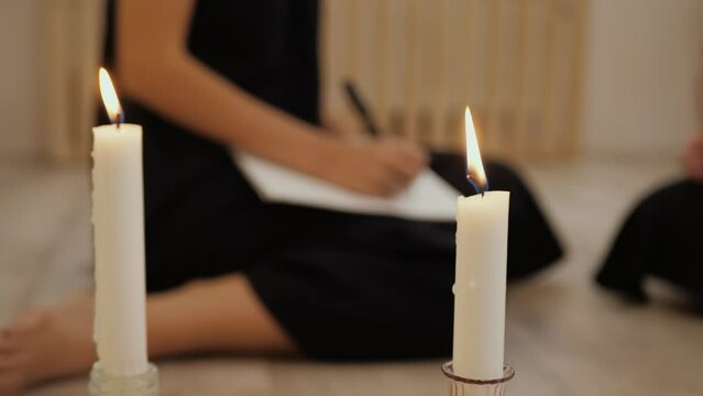 Candle on background of blurred hand of young woman in black writes in notebook, does homework. Concept of lifestyle and work at home. Female writer hand, closeup