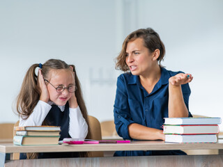 A female teacher yells at a student. Little girl covers her ears with her hands.